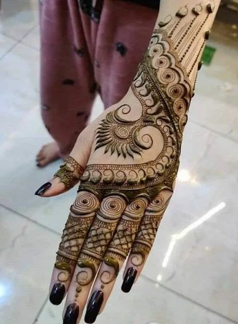 250+ Best Mehndi Designs for Hand Picture and Videos 45 girl wearing trowser and showing her hand with applied mehdi on back hand side